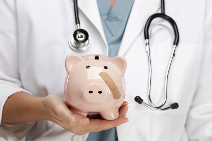 Female Doctor with Stethoscope Holding Piggy Bank with Bandage on Face.