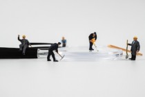 Miniature construction worker is working on a magnifying glass on a white background.