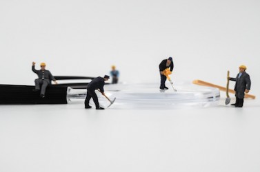Miniature construction worker is working on a magnifying glass on a white background.