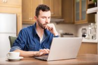 Portrait of a serious guy working on his dining room at home using a laptop