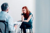 Scared young woman talking to a therapist about abuse in a brigh