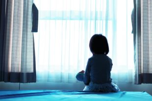 Little baby child sitting on bed playing with the doll in the da