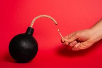 Photo of a round bomb with lit fuse on a red background. Bomb an