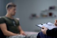 Psychologist making notes during therapy session with sad male s