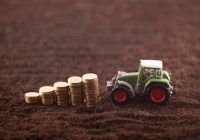 Tractor miniature with coins on fertile soil land