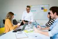 Smiling businessman and colleagues sitting on desk at office