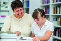 Teacher and girl with syndrome down read a book at library. Educ