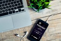 Mobile phone placed on a wooden desk with podcast app in the scr
