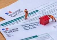 Clamart, France - 6 septembre 2022 : Détail d'un avis d'impôt français sur les taxes foncières avec de petits personnages déplaçant une maison jouet rouge en bois
