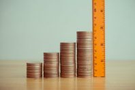 Orange measuring ruler measure growth stack coins on wooden table white wall background copy space. Evaluation assessment of business, investment and financial for successful goal or target.