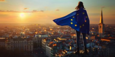 A woman wearing the flag of the European Union e is standing on top overlooking a city during the golden hour