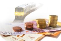 Euro union banknotes and stack of coins, rail train on track out of focus in the background. Cost of transportation concept. Selective focus.. Financial and banking service concept.