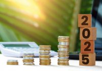 pile of coins and wooden blocks with numbers 2025, calculator, laptop and forest in the background
