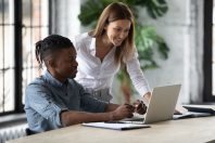 Smiling businesswoman mentor helping new African American employee with software