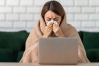 sick woman working from home wrapped in blanket using laptop computer feeling unwell