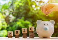 Financial coins stacked with wooden cubes of the year 2026 on a natural background. Piggy bank. New Year 2026 is about finances and saving money.