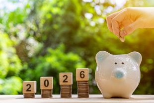 Financial coins stacked with wooden cubes of the year 2026 on a natural background. Piggy bank. New Year 2026 is about finances and saving money.