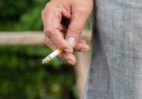 Close up male hand holding a cigarette at outdoor on nature background.