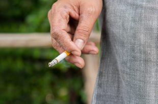 Close up male hand holding a cigarette at outdoor on nature background.