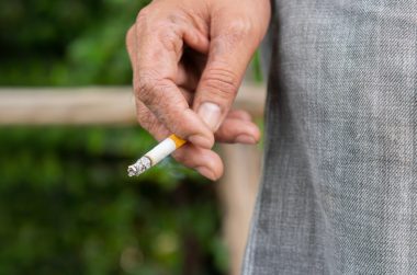Close up male hand holding a cigarette at outdoor on nature background.