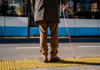 Blind man with a cane stopped on a tactile tile in front of a tram obstacle