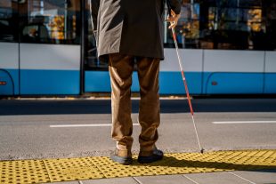 Blind man with a cane stopped on a tactile tile in front of a tram obstacle