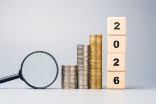 Stacked coins, magnifying glass, and wooden blocks showing 2026, symbolizing future financial goals, investment planning, and economic outlook for the coming year