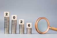 Decreased coins stack with year 2026 blocks and magnifying glass represent financial prediction and economic outlook for the upcoming year