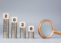 Decreased coins stack with year 2026 blocks and magnifying glass represent financial prediction and economic outlook for the upcoming year