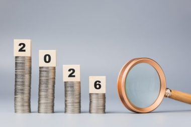 Decreased coins stack with year 2026 blocks and magnifying glass represent financial prediction and economic outlook for the upcoming year