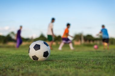 An action picture of a group of kids playing soccer football for exercise in community rural area under the sunset.
