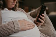 Pregnant woman siting on her sofa using her cellphone