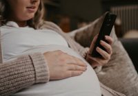 Pregnant woman siting on her sofa using her cellphone