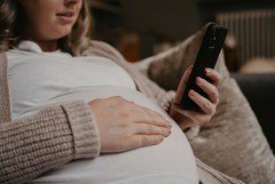 Pregnant woman siting on her sofa using her cellphone