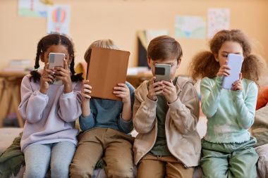 Group of young children holding smartphones and hiding faces