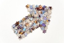 Thick arrow pointing to the left and up, made from plenty of colorful jigsaw puzzle pieces separated on white background.